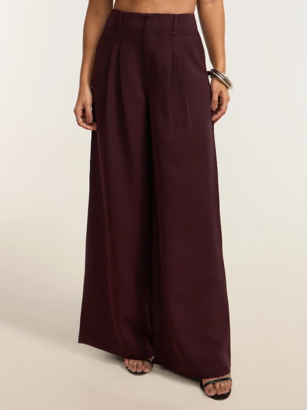 Modelo mostrando detalhes de uma calça wide leg alfaiatada com pregas duplas bordô.